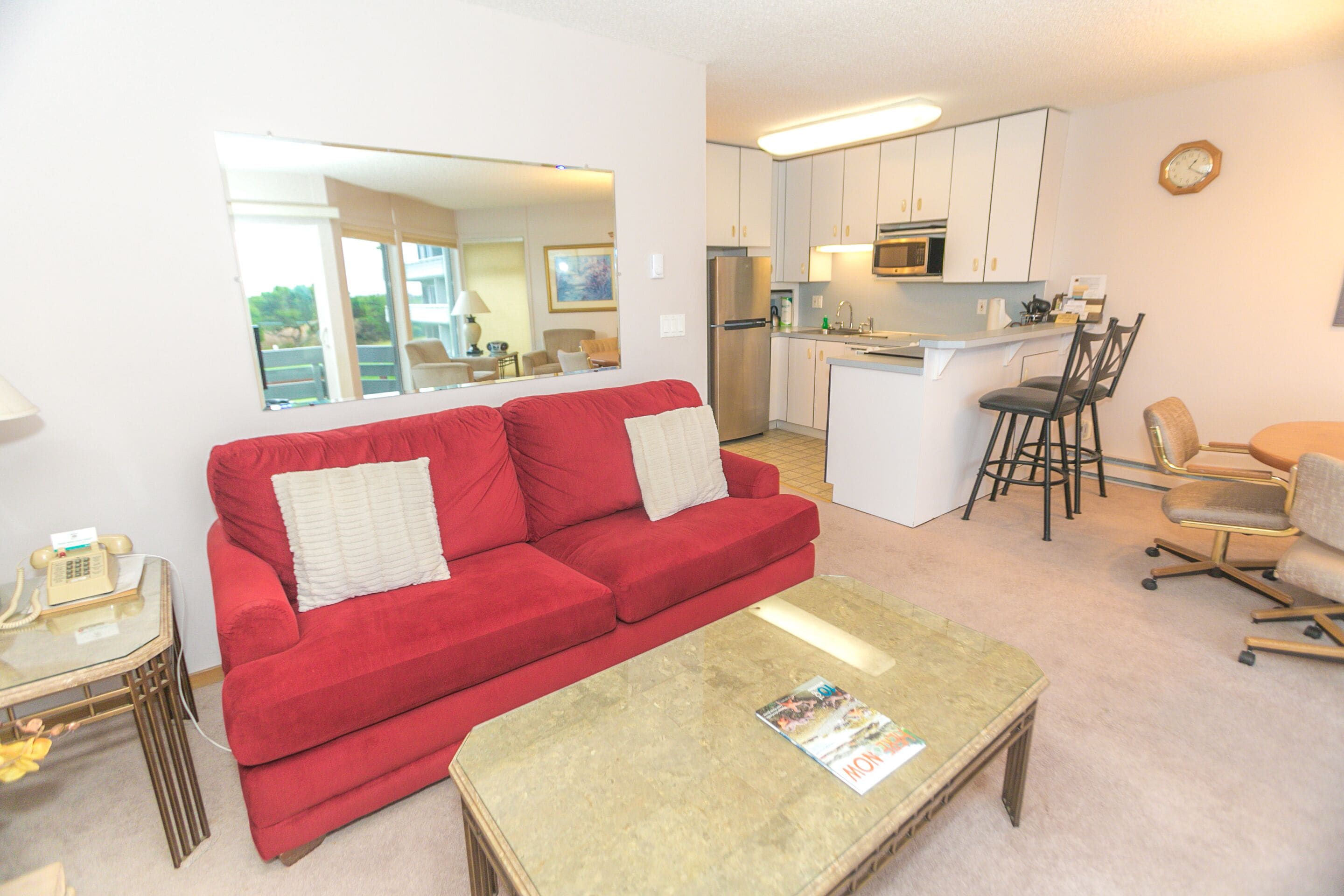 A compact living space with a red sofa, a coffee table, a kitchen area with a refrigerator and microwave, and a dining area with chairs.