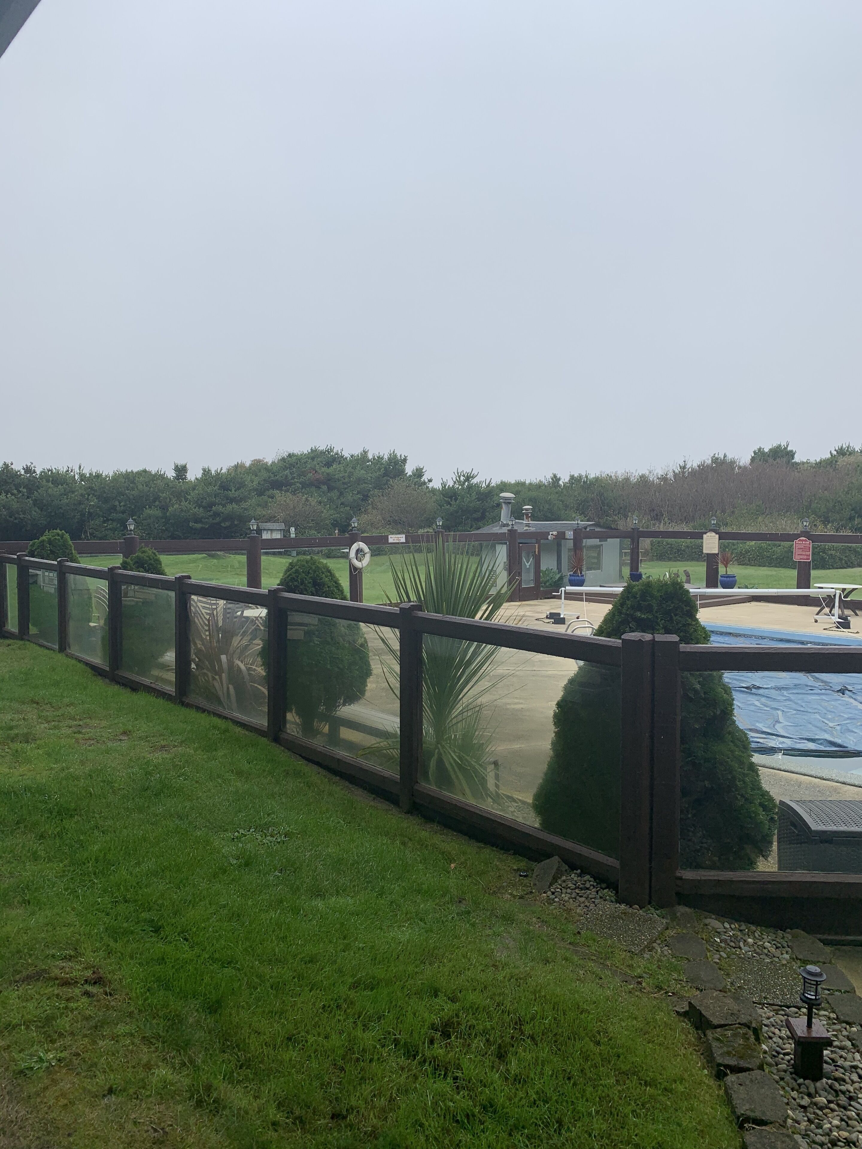 A fenced outdoor area with a pool, a small building, and a grassy field.
