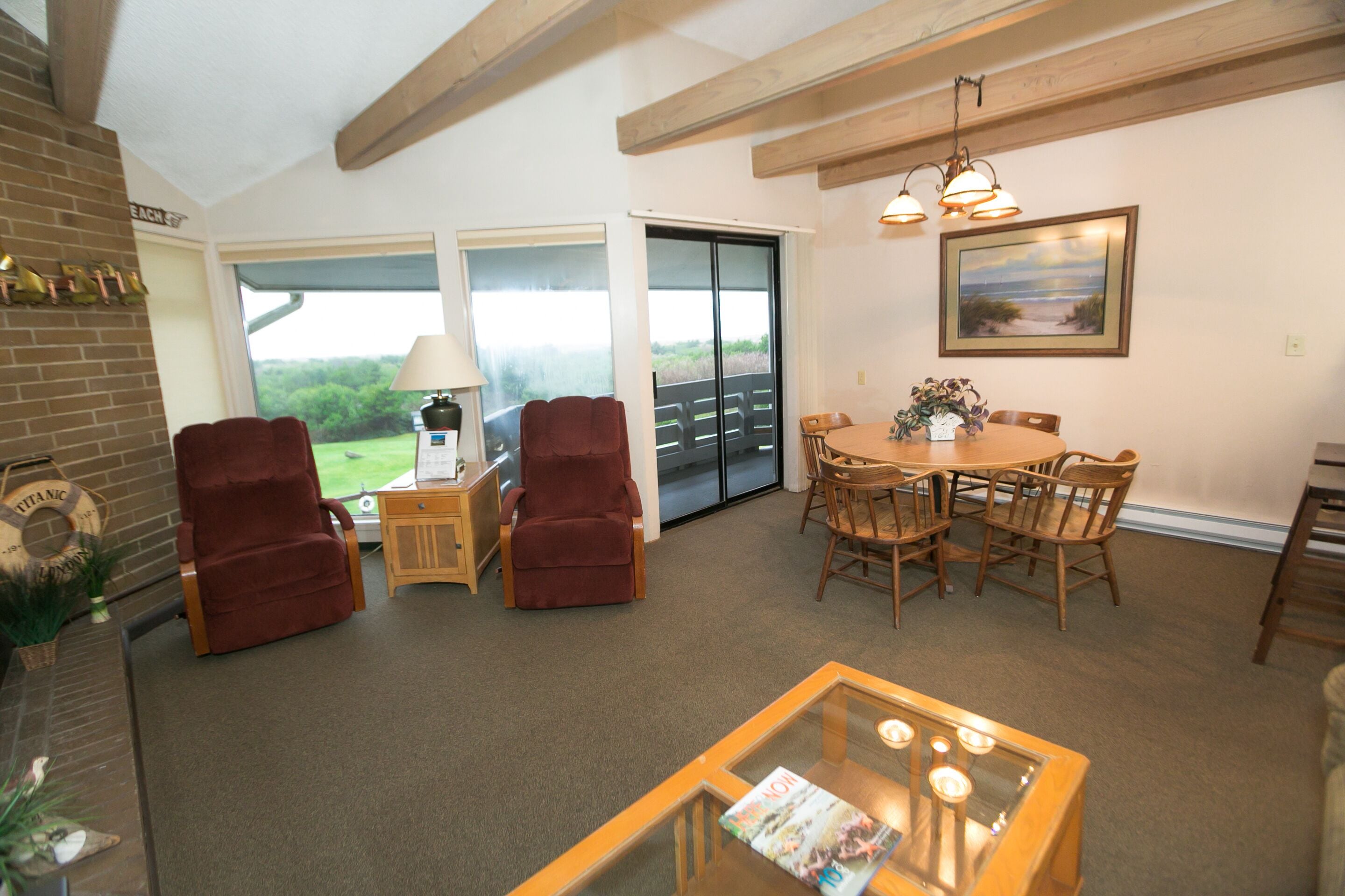 A spacious living room with a fireplace, two red armchairs, a glass coffee table, and a dining area with wooden chairs and a table.