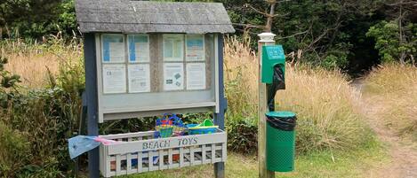 A wooden information kiosk with a roof, surrounded by grass and trees.