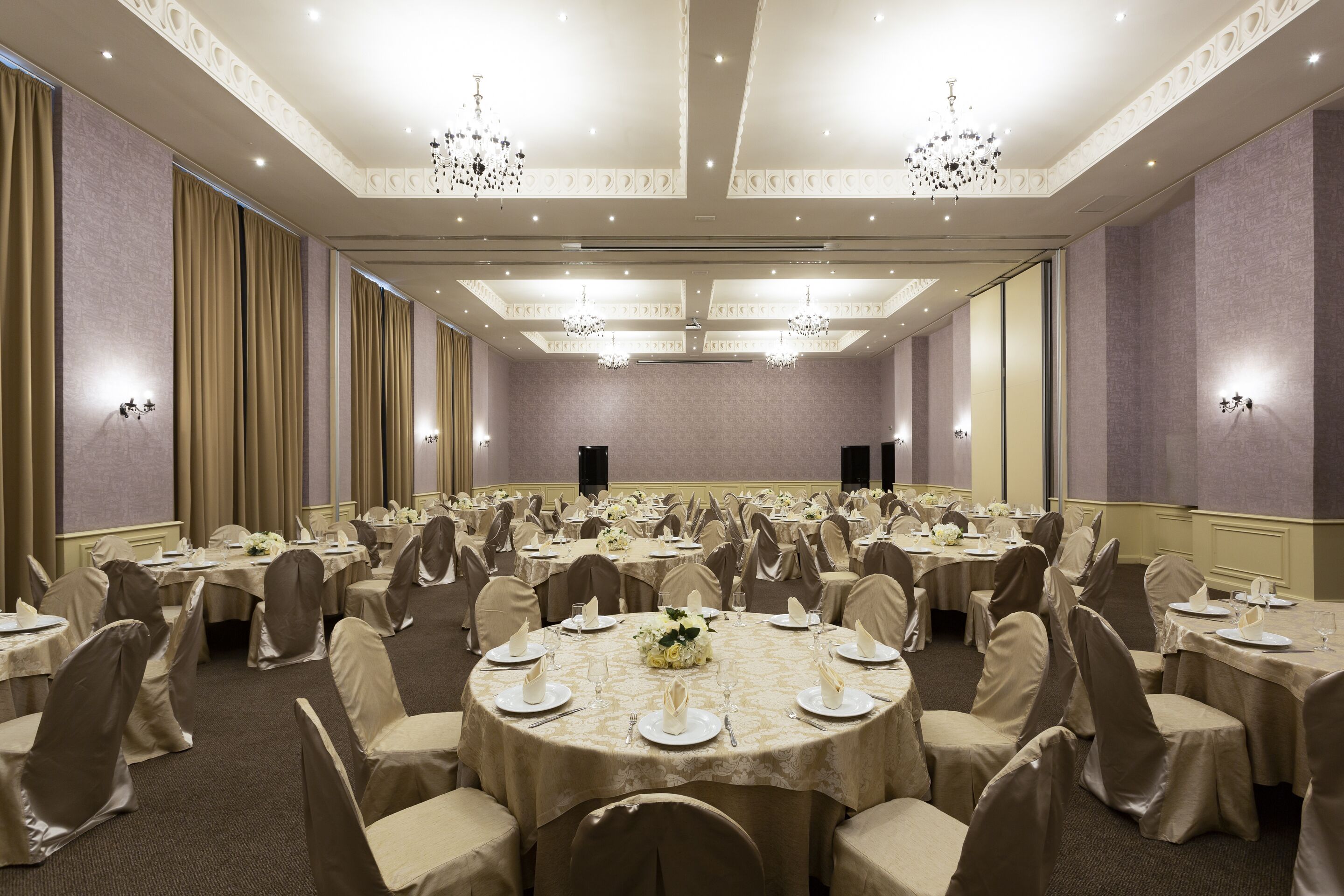 A large banquet hall with round tables, chairs, and chandeliers.