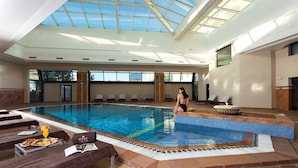 An indoor swimming pool with a skylight, lounge chairs, and a towel service area. - Hotel Concorde Les Berges du Lac (Tunis)