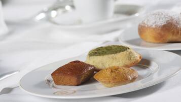 Una mesa con platos de pasteles, un vaso de una bebida amarilla y una taza blanca.