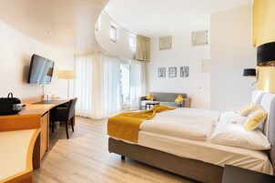 Una habitación de hotel moderna con cama, escritorio, silla y televisión montada en la pared.