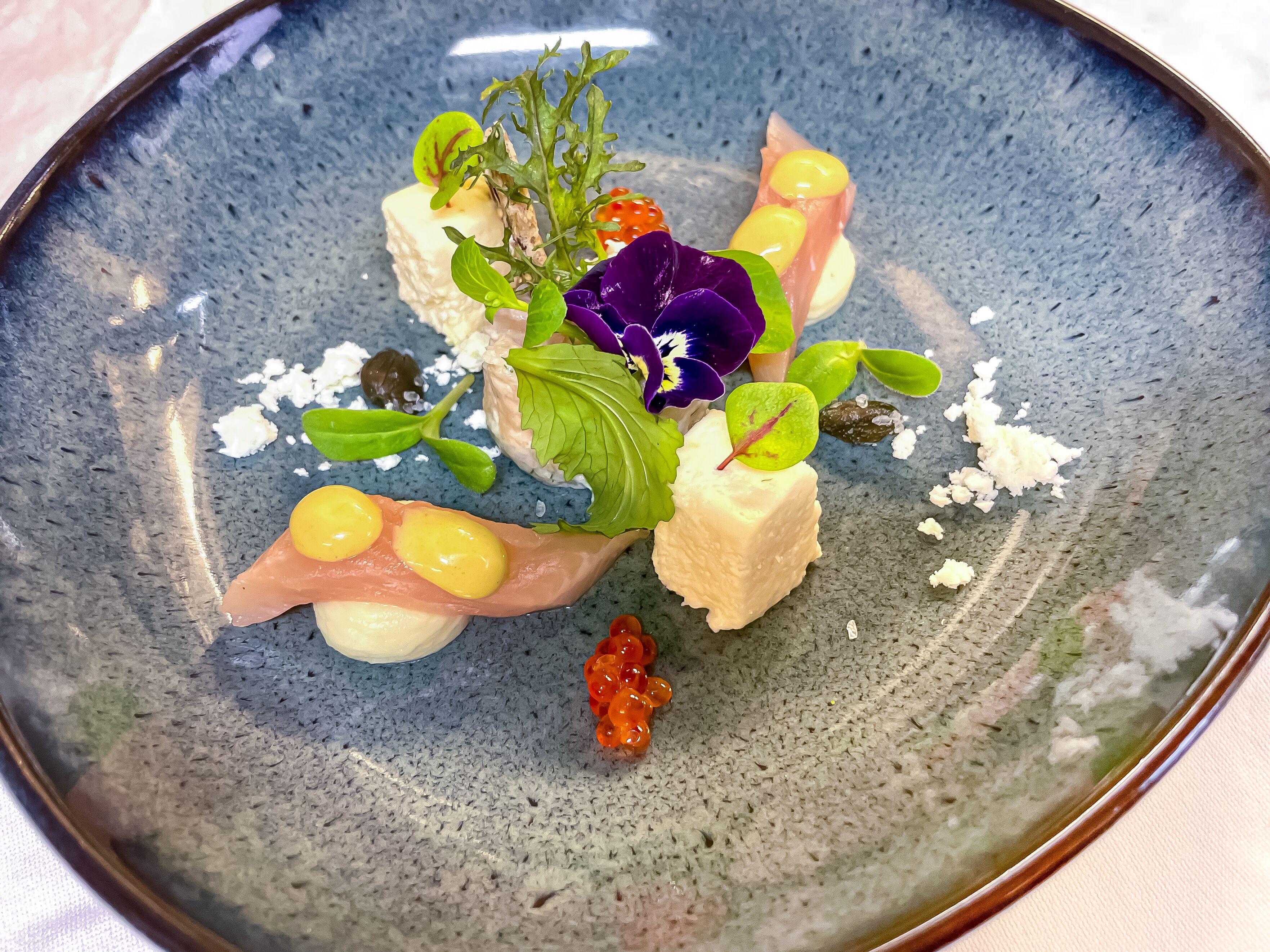 Ein Teller mit verschiedenen Speisen, darunter Käse, Salat und möglicherweise Lachsrogen oder Kaviar.