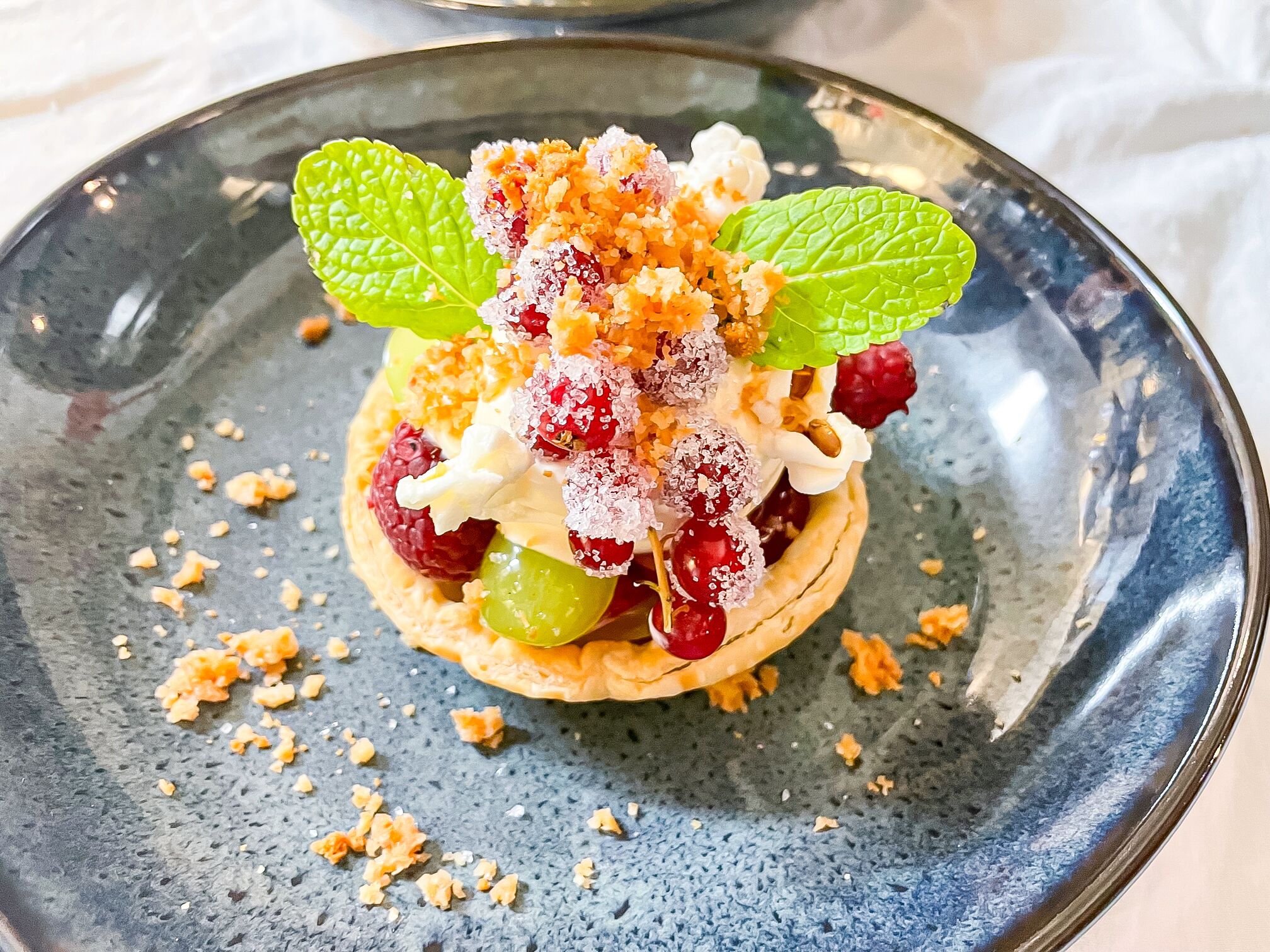 A dessert on a blue plate with raspberries, green grapes, and mint leaves.