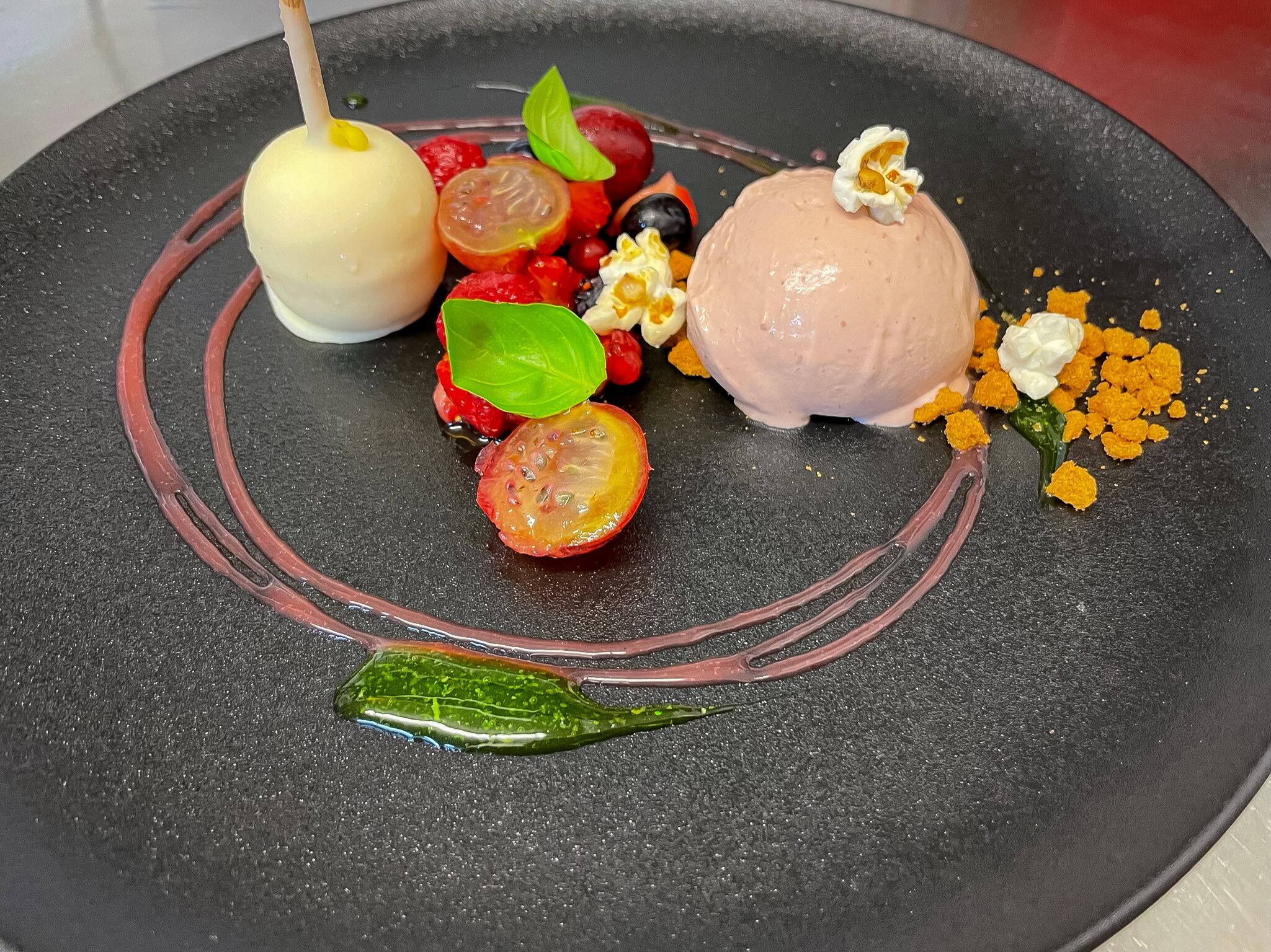 Un plato de postre con diversas frutas y una bola de helado.