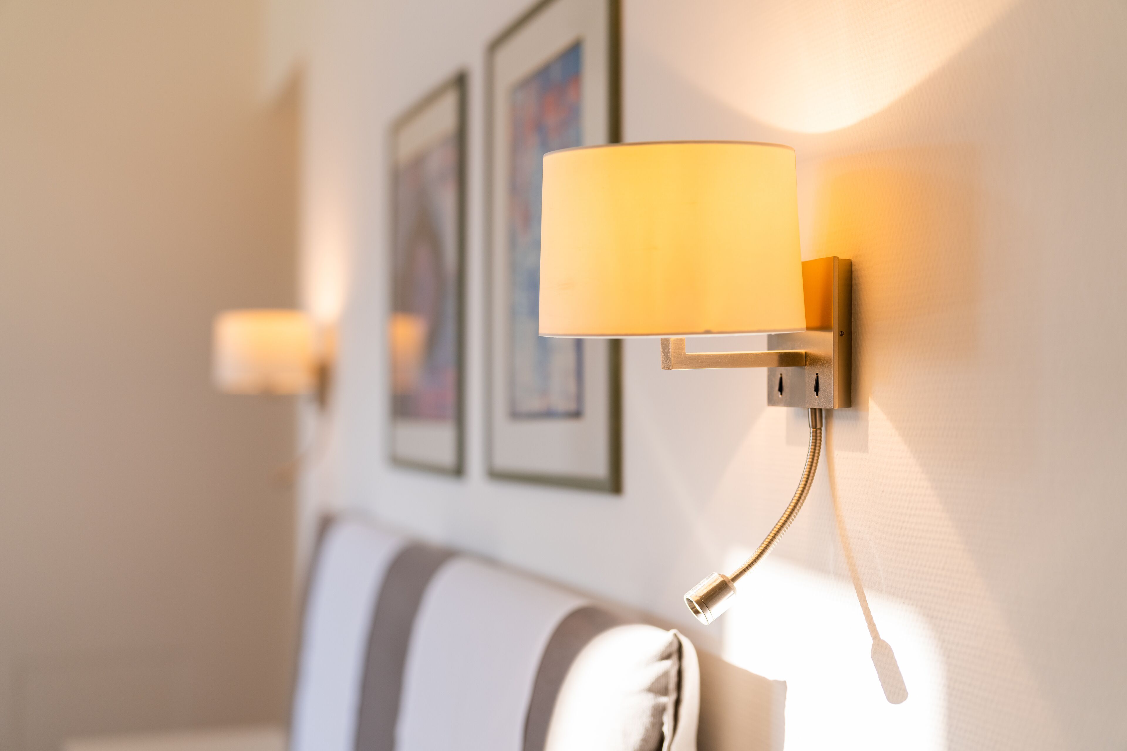 Eine Wandleuchte mit zylindrischem Lampenschirm, eine weiße Wand mit gerahmten Kunstwerken und ein gestreiftes Sofa.