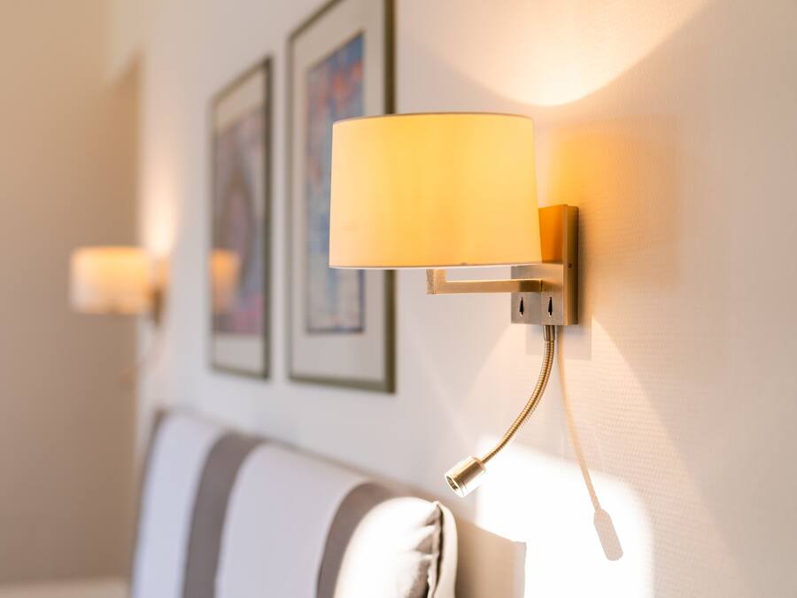 Eine Wandleuchte mit zylindrischem Lampenschirm, eine weiße Wand mit gerahmten Kunstwerken und ein gestreiftes Sofa.