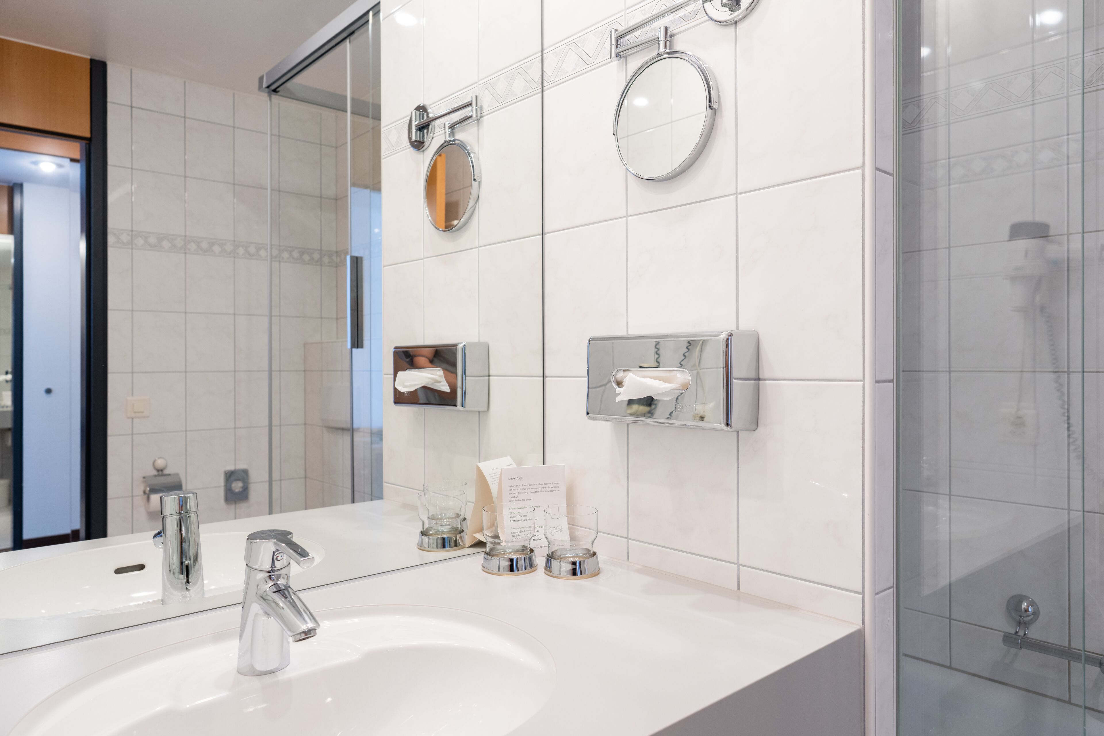 A modern bathroom with a large mirror, a sink, and a glass shower enclosure.