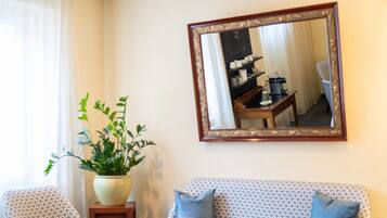 A living room with a sofa, a coffee table, a potted plant, and a mirror reflecting a dining area with a table and chairs.