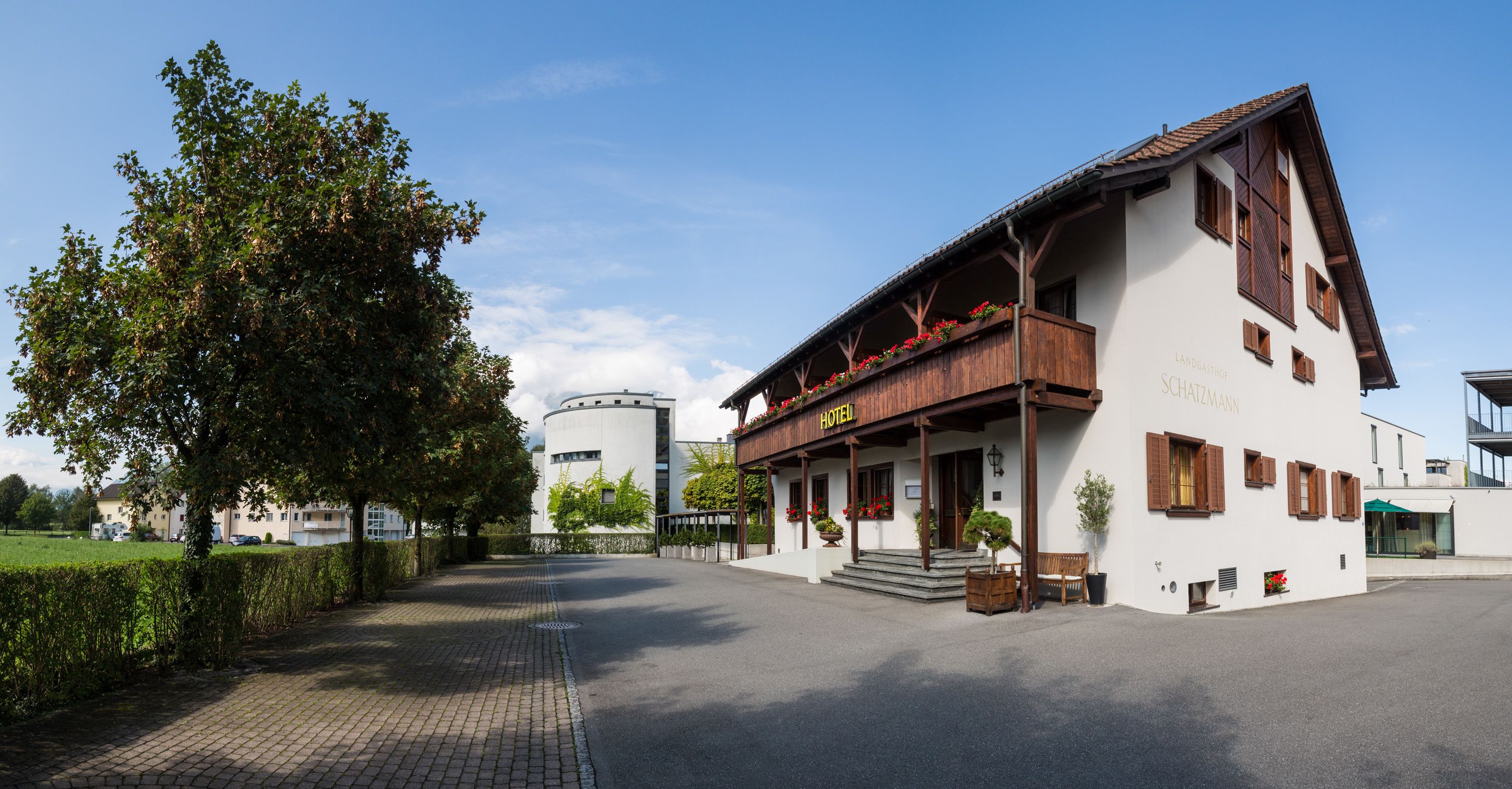 A hotel with a white facade, wooden balcony, and steps leading to the entrance.