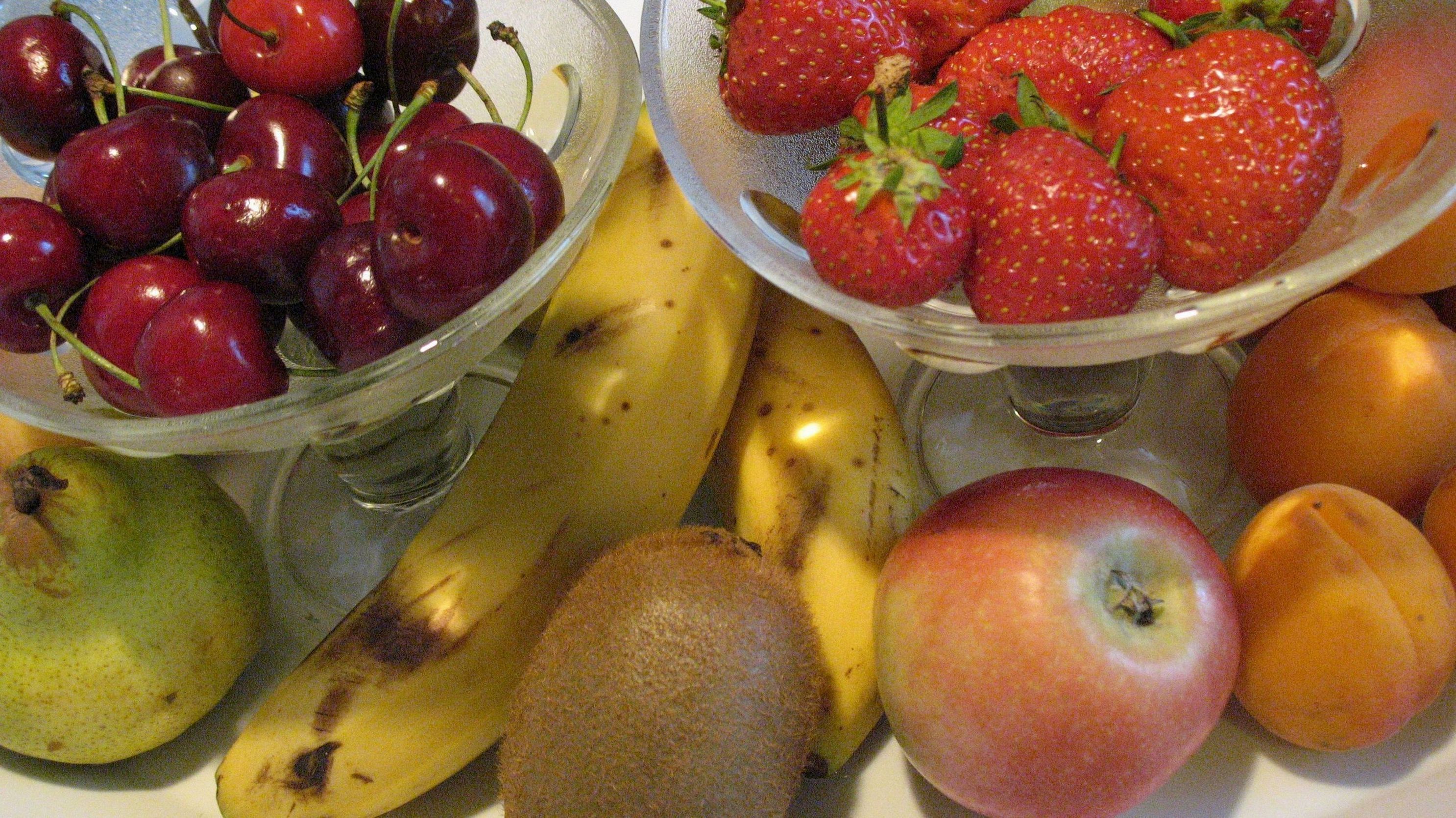 A fruit bowl containing cherries, strawberries, a banana, a pear, an apple, and peaches.