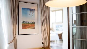 A room with a framed landscape painting, a wooden bench, and a window with curtains.
