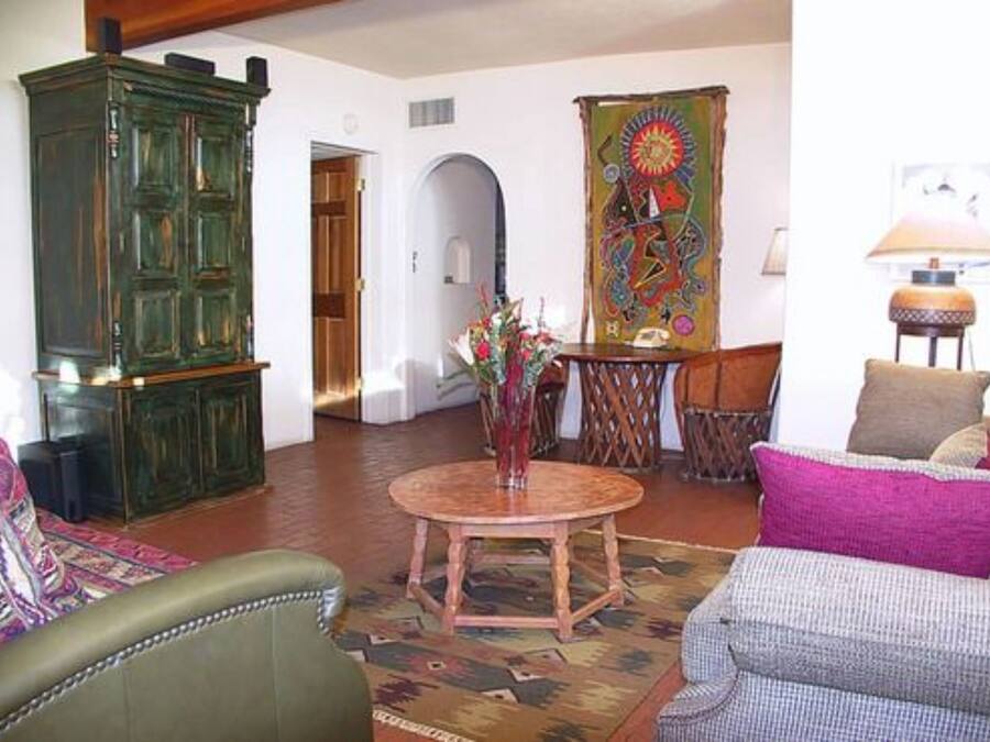 A living room with a green cabinet, a round wooden table, a colorful tapestry, and a lamp.