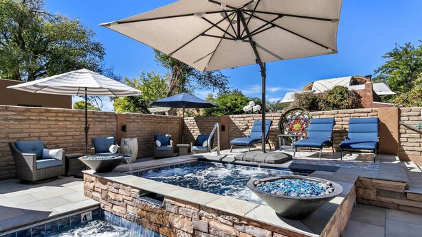 A hot tub surrounded by stone walls, outdoor seating, and umbrellas. - Casas de Suenos Old Town Historic Inn, an Ascend Collection Hotel (Albuquerque)