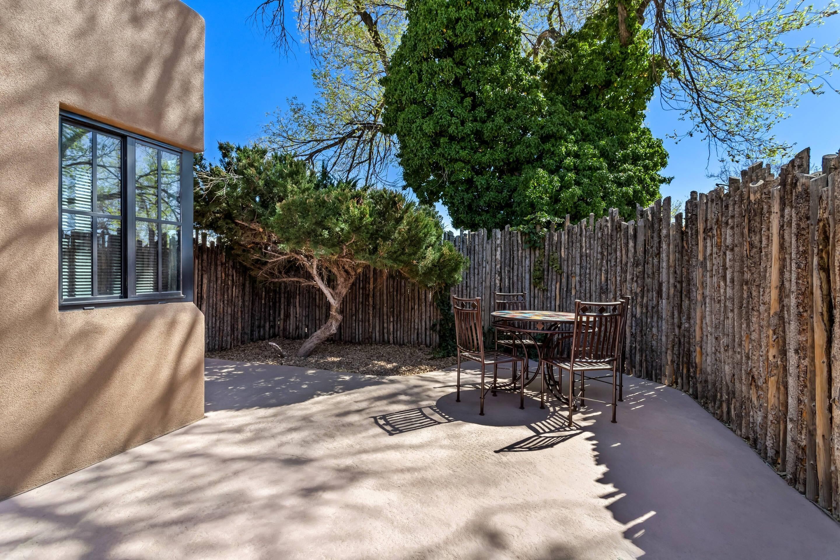 A patio with a table and chairs, a wooden fence, and a tree.