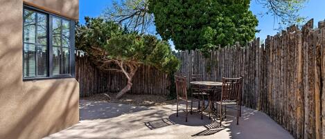 A patio with a table and chairs, a wooden fence, and a tree.