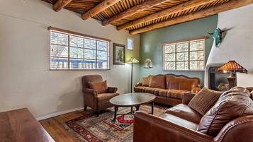 A cozy living room with a wooden ceiling, leather sofas, a round coffee table, and a patterned rug.