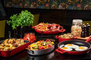 A variety of dishes including roasted potatoes, sautéed vegetables, and eggs in a pan, with a potted plant and condiments in the background.