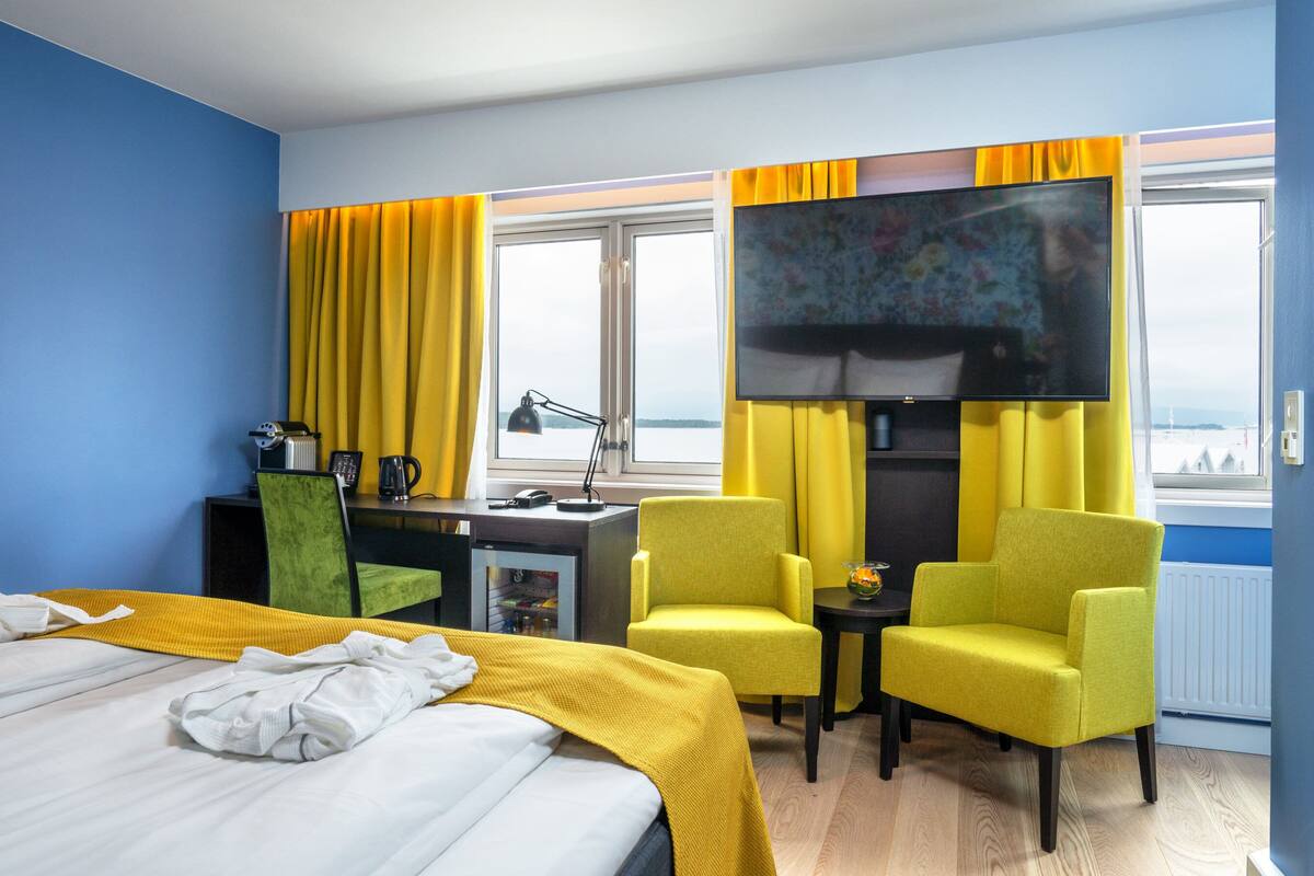A hotel room with a bed, a desk, a television, and two chairs.
