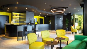 Un espace bar moderne comprenant un comptoir, des tabourets de bar et un coin salon avec des chaises jaunes et vertes.