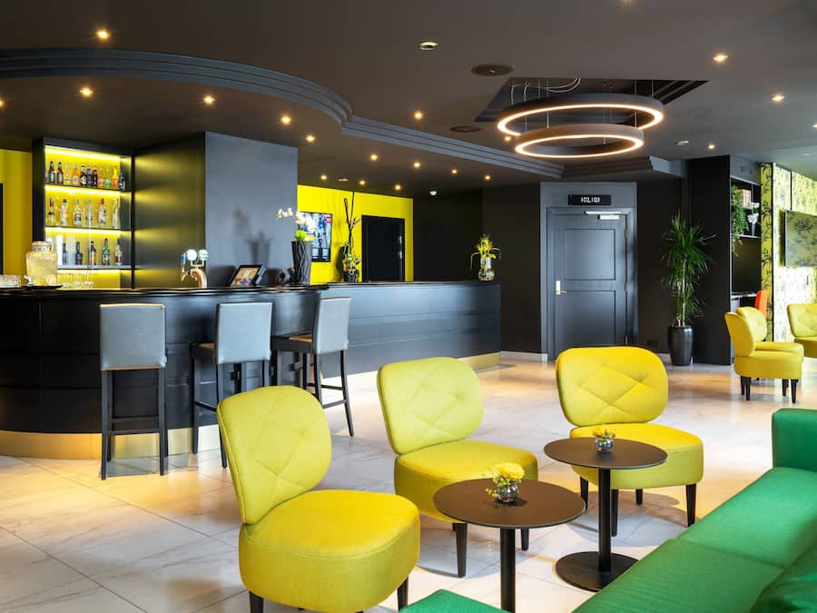 Zona de bar moderna con barra, taburetes y un área de estar con sillas amarillas y verdes.