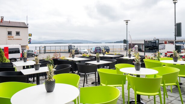 Un espace extérieur aménagé avec des tables et des chaises, une vue sur la mer et des véhicules garés.