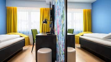 A hotel room with two beds, a desk with a lamp, a chair, and a large window with yellow curtains.