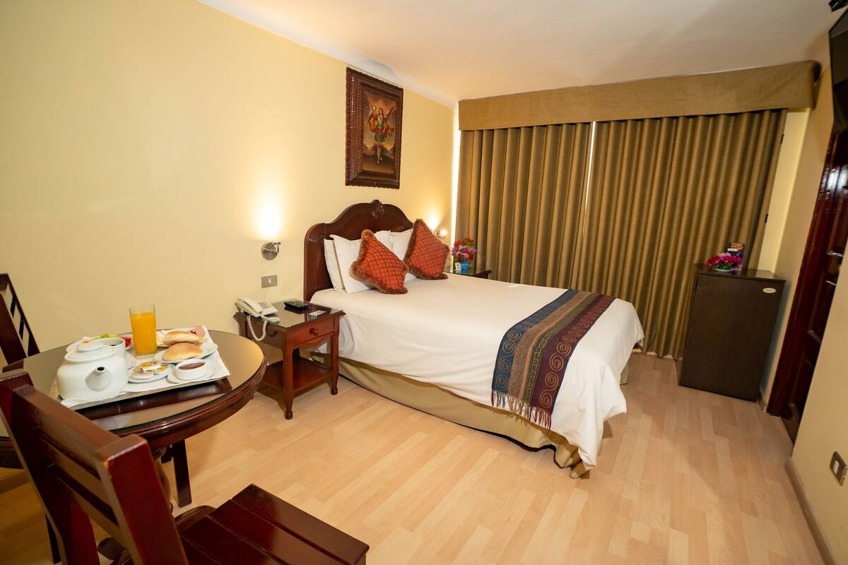 A hotel room with a bed, bedside table, and a small desk with breakfast items.