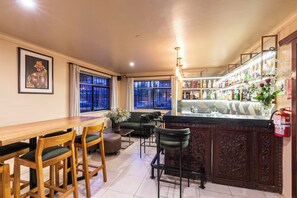 A bar area with a wooden counter, bar stools, and a fire extinguisher. There are chairs and a sofa in the seating area. - Agustos Cusco (Cusco)