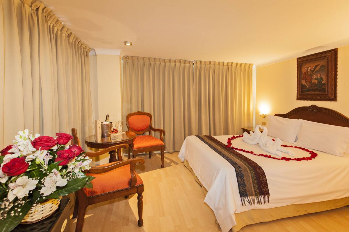 A hotel room with a bed, a chair, a table with a vase of flowers, and curtains.