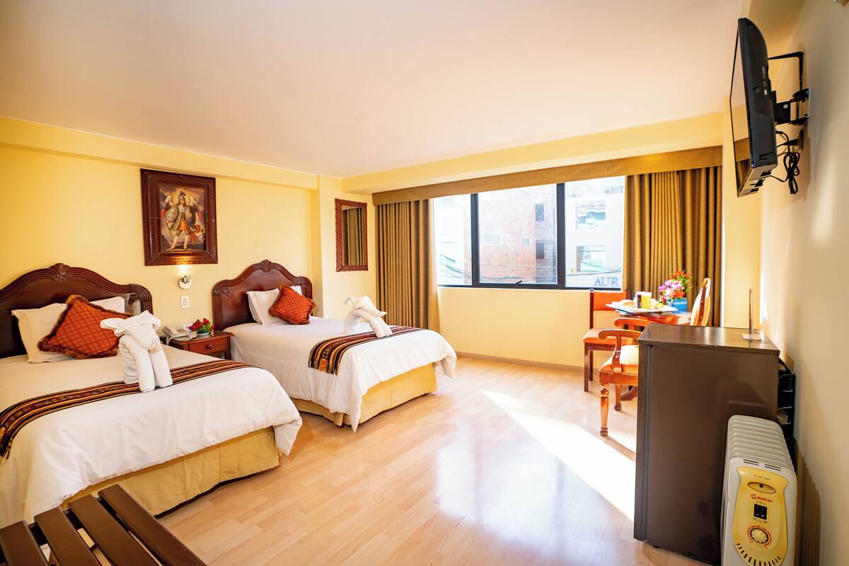 A hotel room with two beds, a desk, a chair, a television, and a window with curtains.