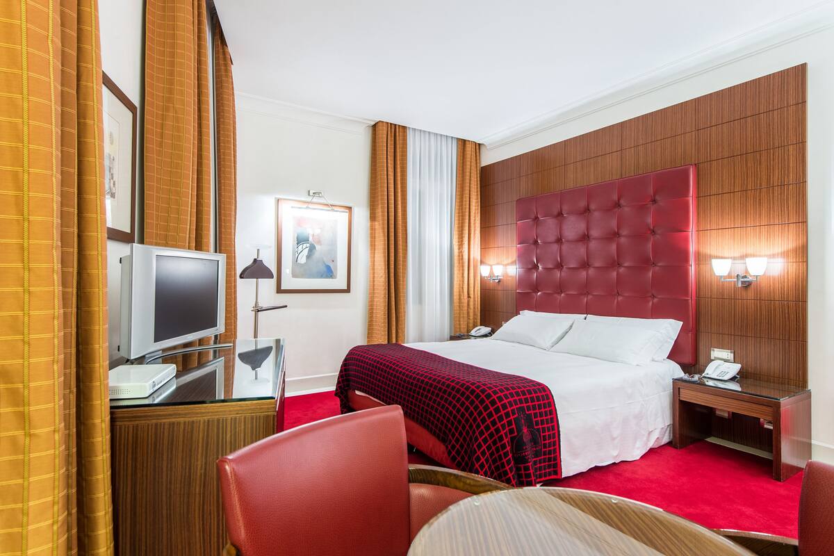 A hotel room with a large bed, a desk with a computer, a chair, and a TV.