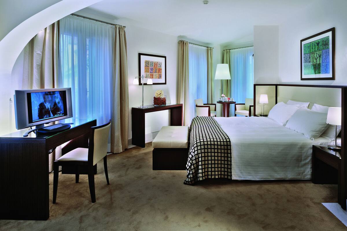 A hotel room with a bed, desk, chair, TV, and artwork on the walls.
