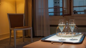 A dining table with a tray holding two glasses of white wine and a plate of food, a chair, a lamp, and a window with a view of a tower.