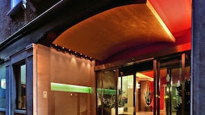 A hotel entrance with a glass facade, a red awning, and a staircase leading up to the entrance.
