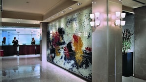 A lobby with a reception desk, a colorful mosaic wall, and a potted plant.