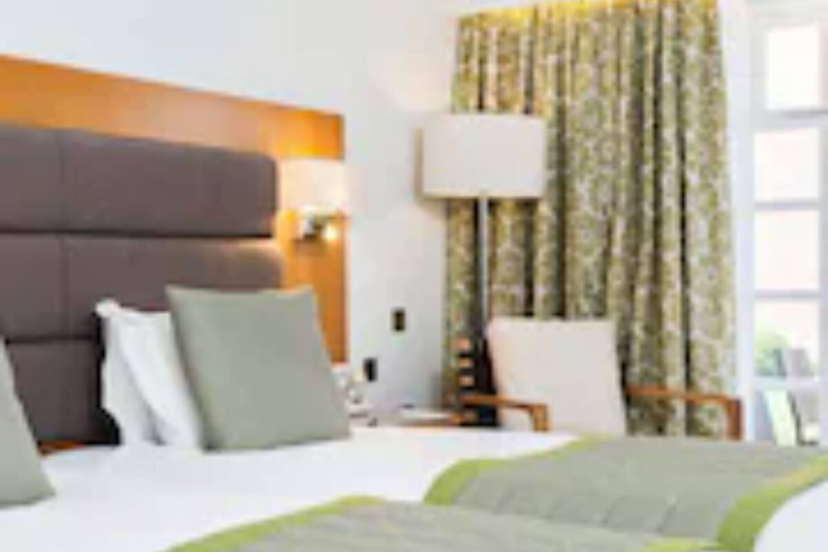 A hotel room with two beds, a large headboard, a nightstand, a lamp, and a window with curtains.