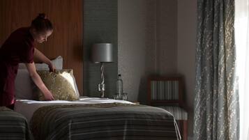 A hotel room with a bed, a bedside table, a lamp, and a window with curtains.