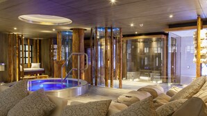 Un área de spa moderna con un jacuzzi, asientos con cojines estampados y una zona de ducha con paredes de vidrio.