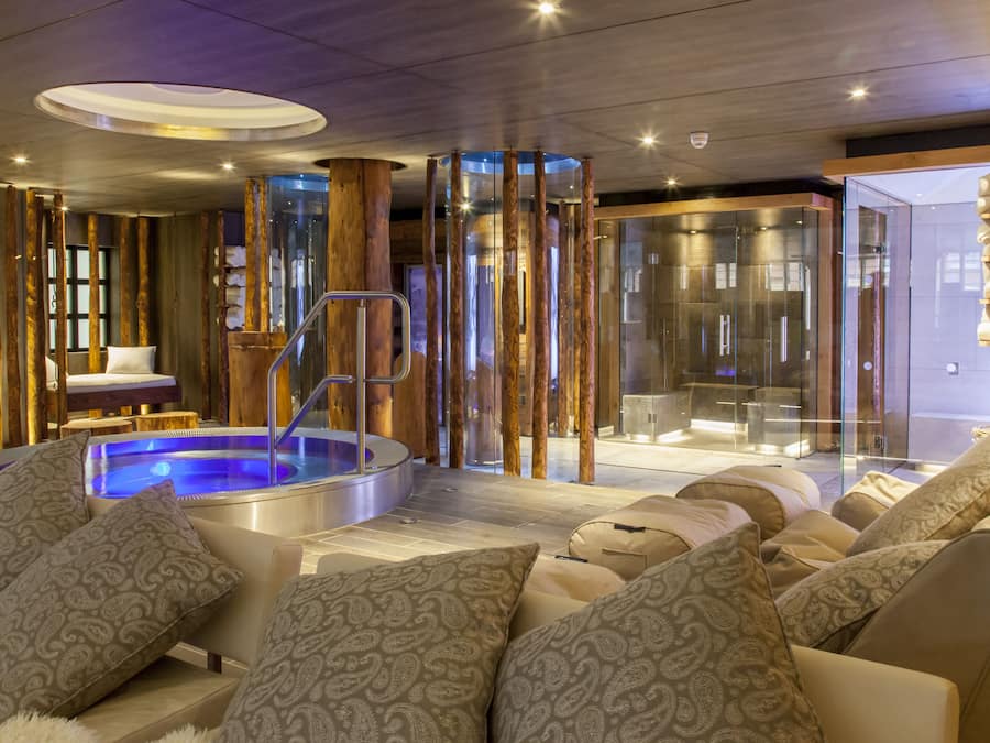 A modern spa area with a hot tub, seating with patterned cushions, and a glass-enclosed shower area.