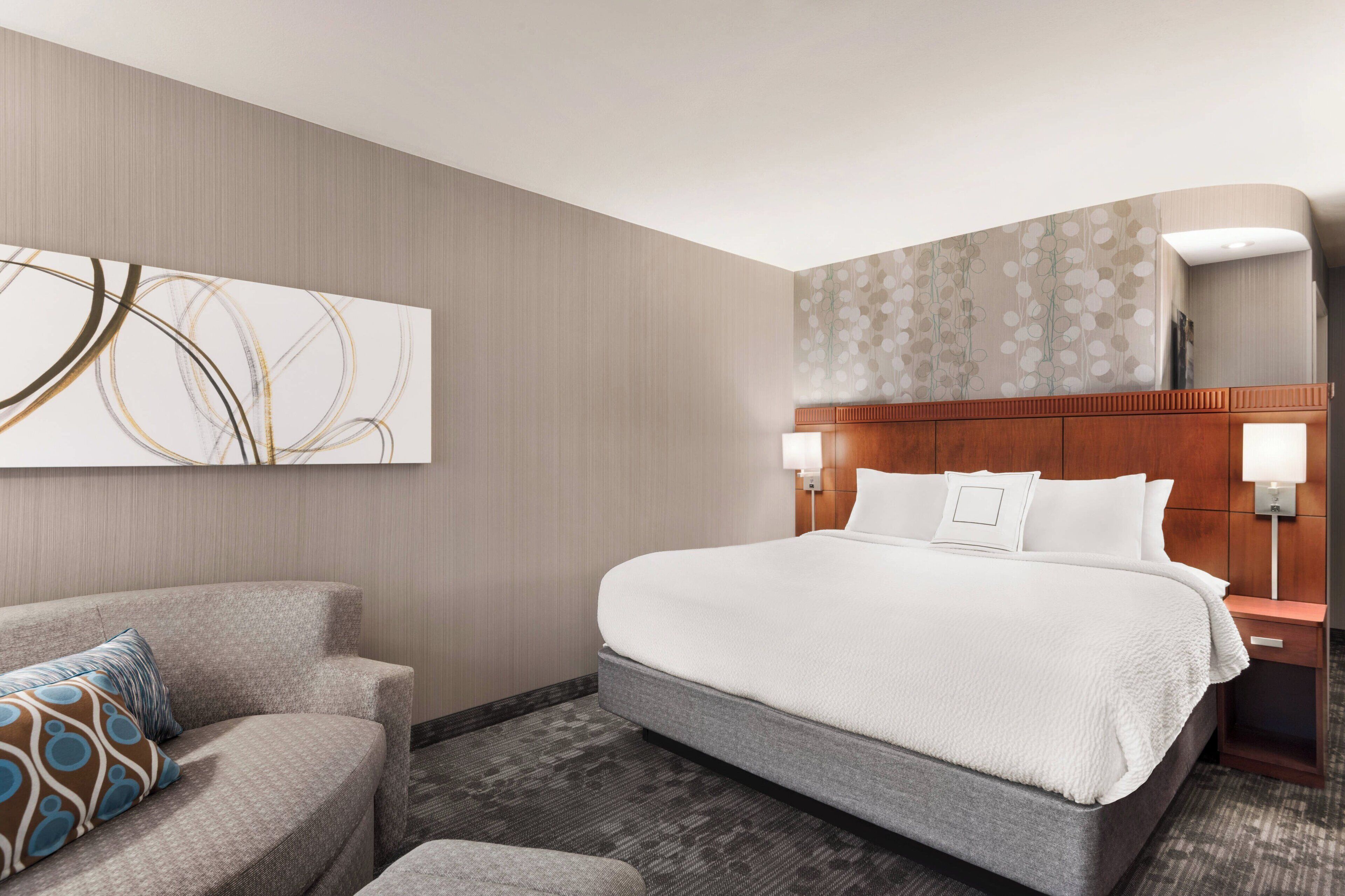 Ein Hotelzimmer mit einem großen Bett, einer Schlafcouch, einem Wandbild und einem Nachttisch mit Lampe.
