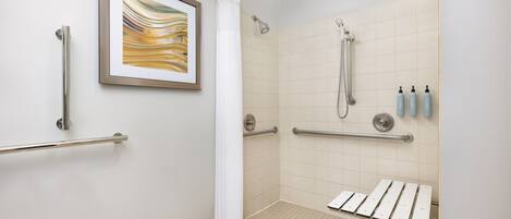 A handicap-accessible shower area with grab bars, a framed artwork, and a white shower curtain.