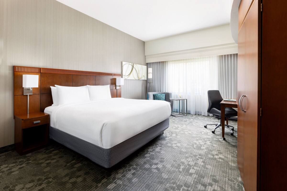 Une chambre d’hôtel avec un grand lit, un bureau, une chaise et une armoire.