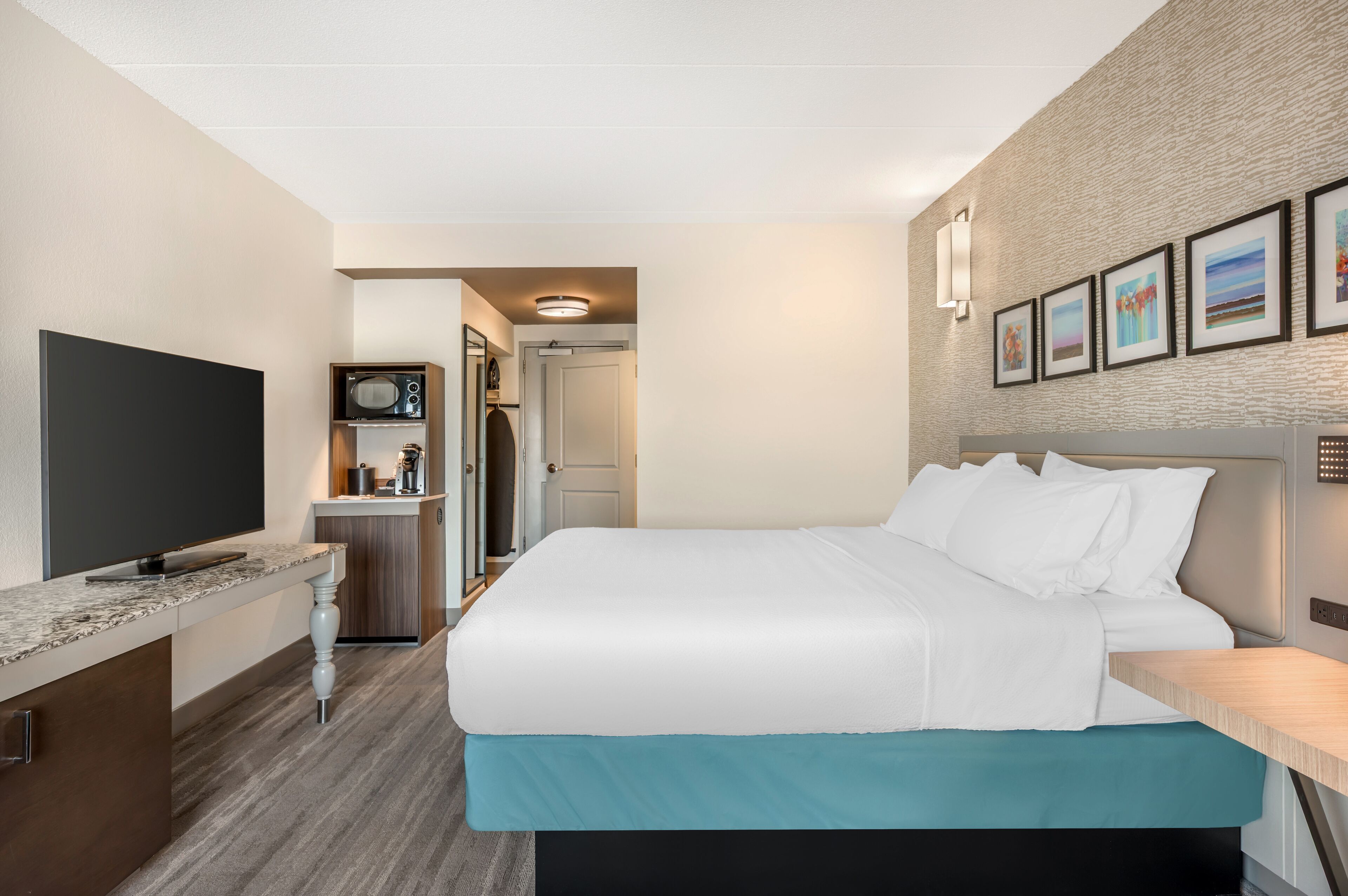 Habitación de hotel con cama, televisión de pantalla plana, kitchenette y puerta que da a otra habitación.