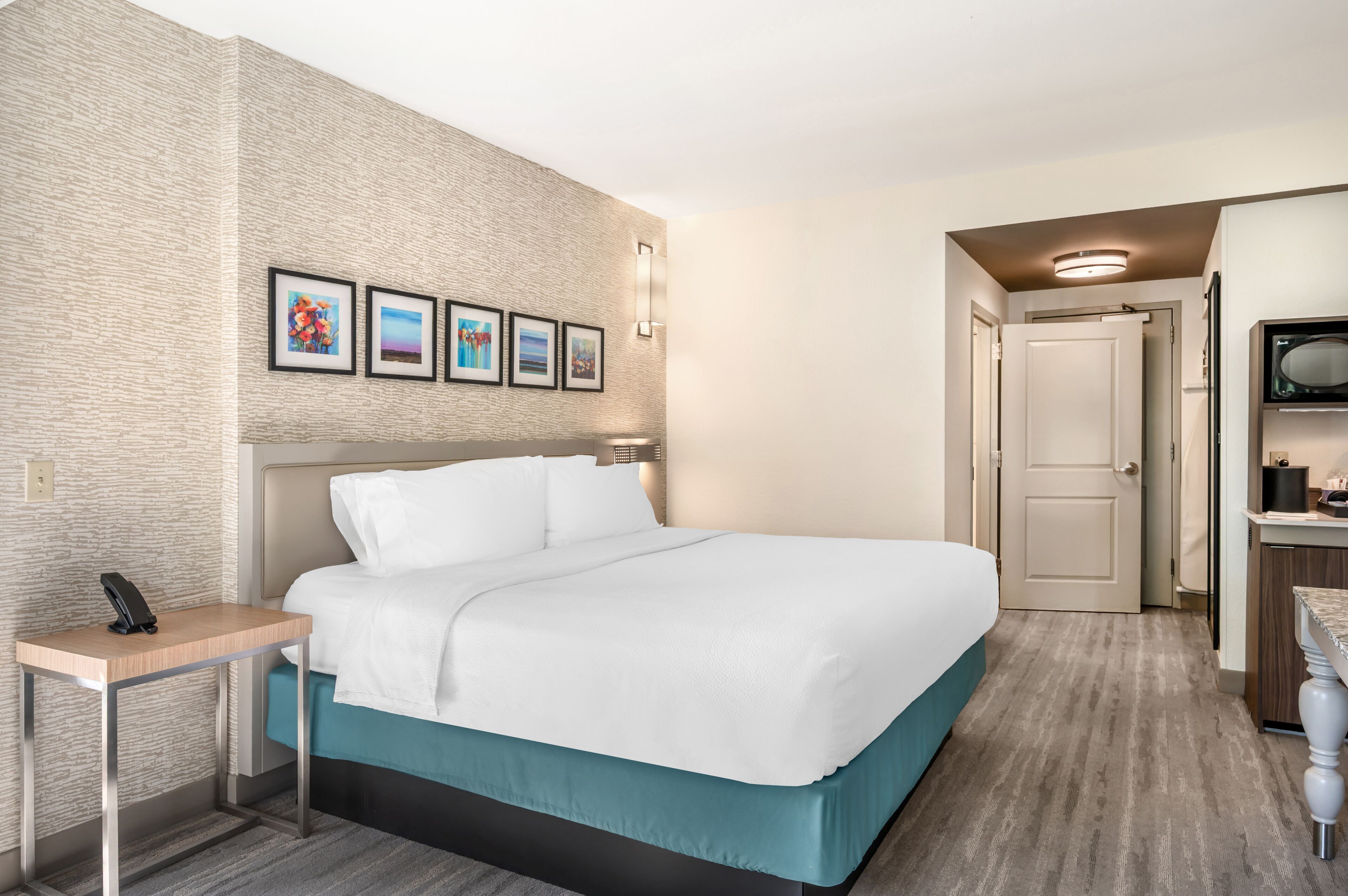 A hotel room with a large bed, a bedside table with a phone, a wall-mounted light, and framed pictures above the bed.