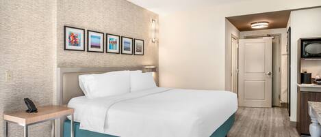 A hotel room with a large bed, a bedside table with a phone, a wall-mounted light, and framed pictures above the bed.