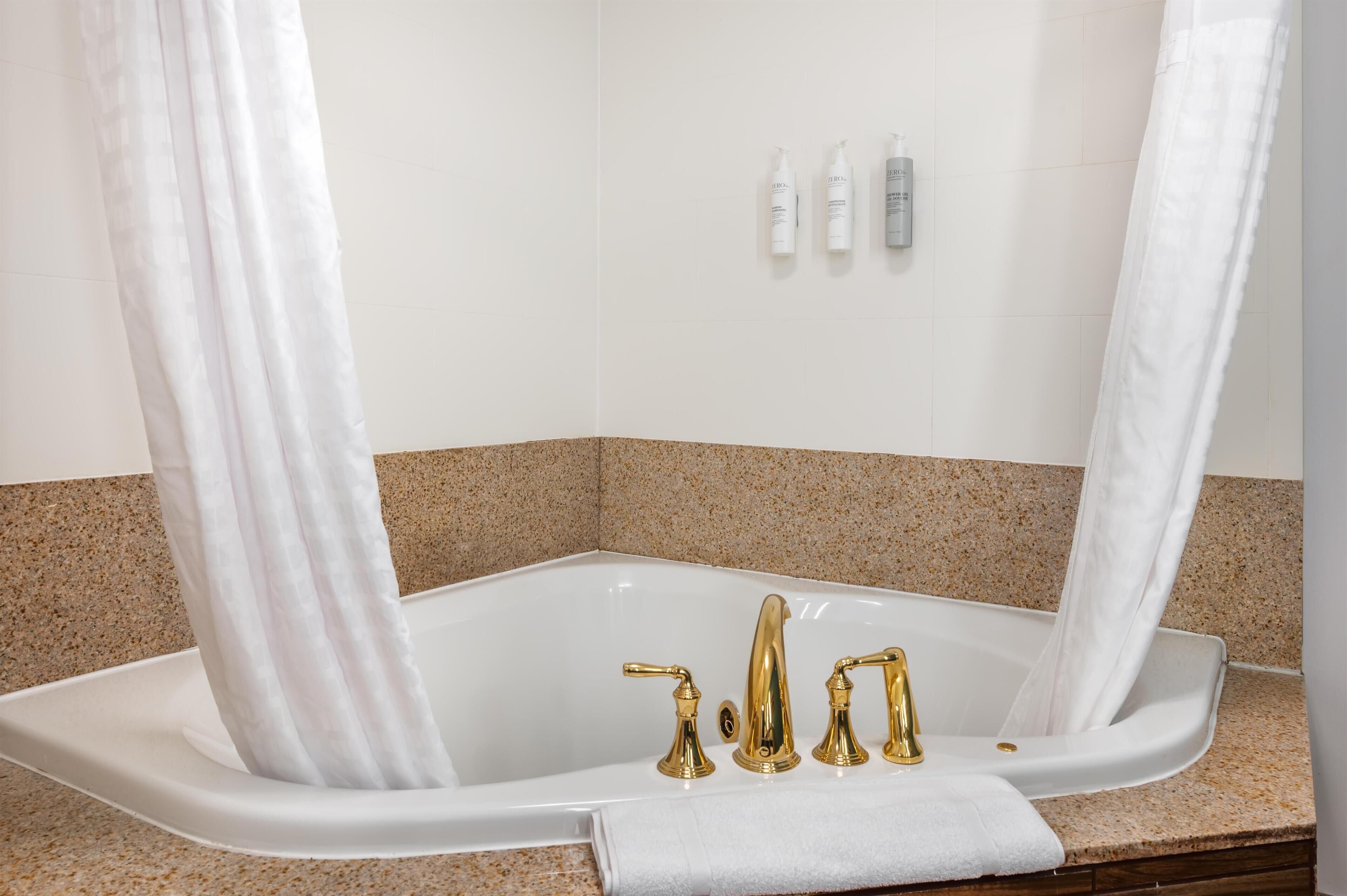 A modern bathroom with a freestanding bathtub, gold faucets, and a shower curtain.
