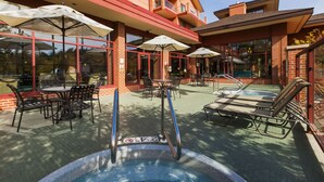 An outdoor patio with tables and chairs, a pool area, and a glass-enclosed building with red accents. - Hilton Garden Inn Wisconsin Dells (Wisconsin Dells)